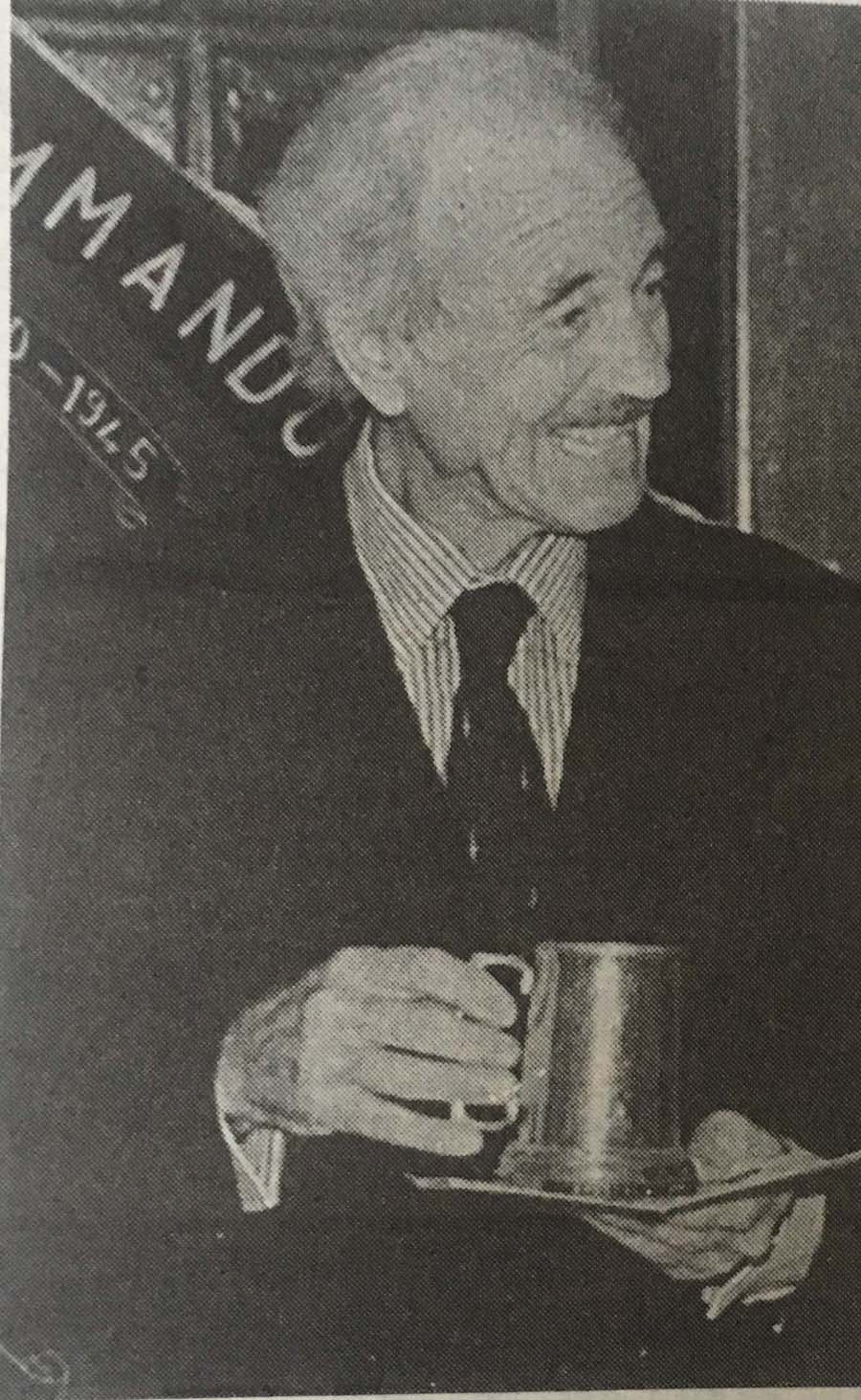 Leslie Callf in 1988, smiling and holding a pewter tankard beneath a Commando Association banner
