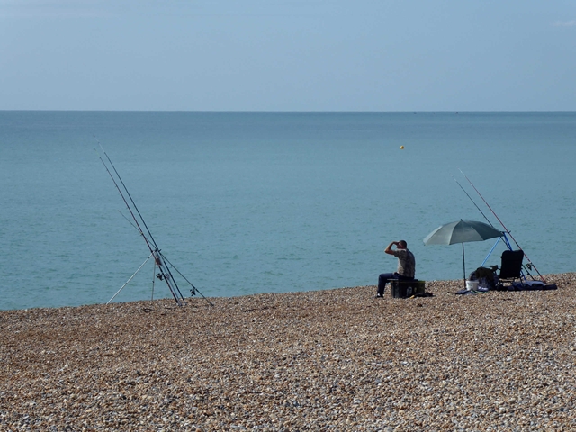 An angler casting from the shingle at Seaford with the chalk cliffs of Seaford Head behind
